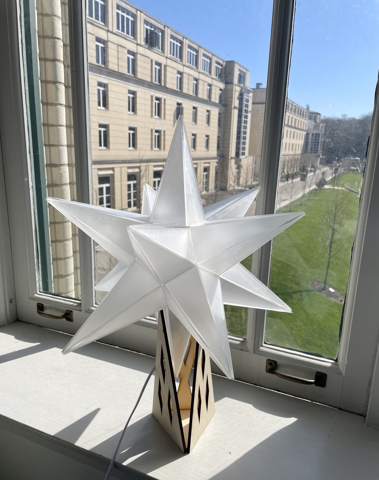 A handmade white paper star lamp on a sunny windowsill overlooking a campus street