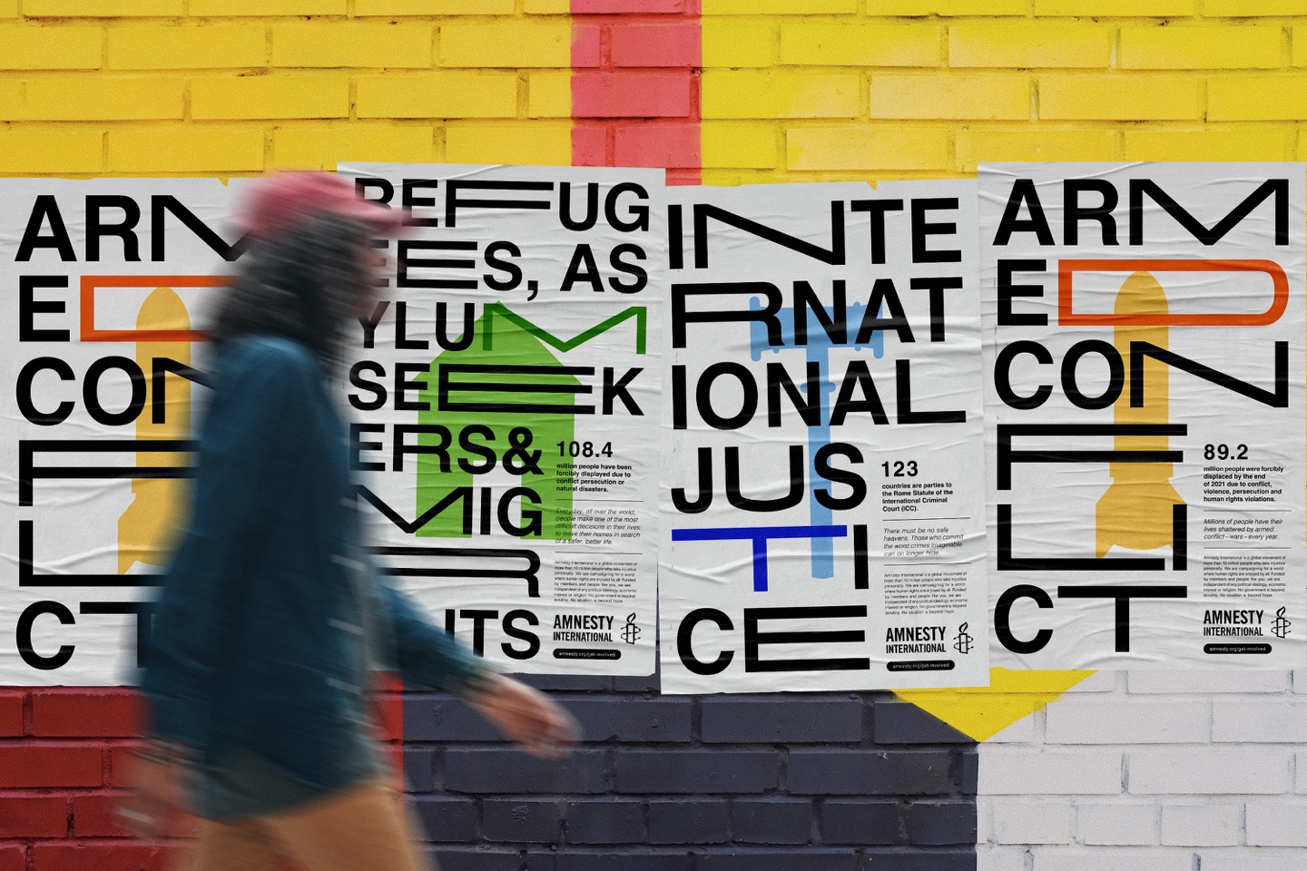 Amnesty International poster series pasted on a painted brick wall as a person walks past (Medium article)